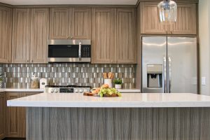 A beautiful modern kitchen with sparkling white countertops, light-brown wood cabinets, and a textured backsplash.