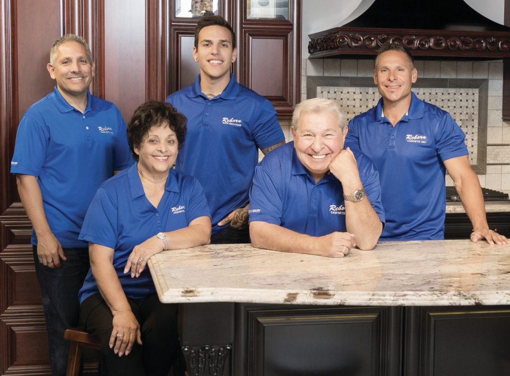 Five owners of Reborn Cabinets wearing blue polo shirts stand in an updated kitchen smiling for the camera.