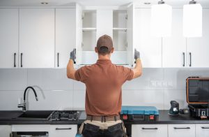 A cabinetmaker installing white kitchen cabinets 