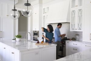 A beautiful kitchen with white cabinets and countertops, and a couple working in the kitchen.
